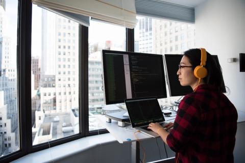 Developer coding on a multi-monitor setup with a view of the skyline outside