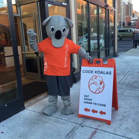Person in Koala costume stands outside an office door with a sign that reads eat, drink, learn to code