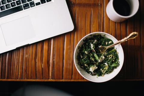 Bowl of greens next to a laptop and a coffee cup