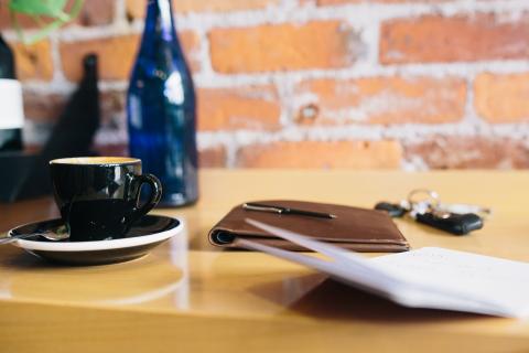 Coffee cup, note pads, keys and a glass bottle on a wooden surface