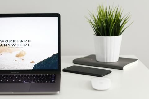 Open laptop on a table with a mouse, mobile device and small potted plant