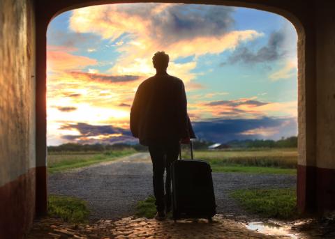 Man walking through an archway with luggage at sunset