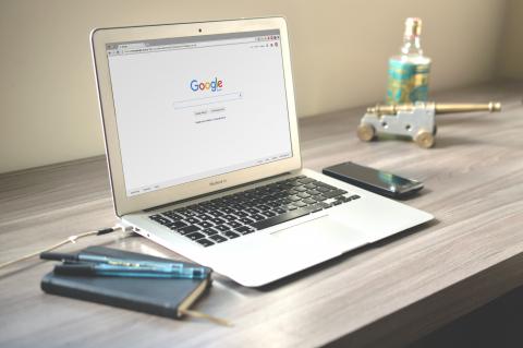 Laptop, notepad, mobile device, alcohol, and a mini-canon paperweight on a desk