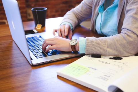 Working on a laptop with reference material on a wooden desk