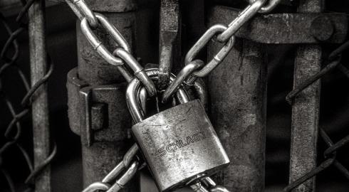 black and white image of a padlocked chain wrapped around a fence gate
