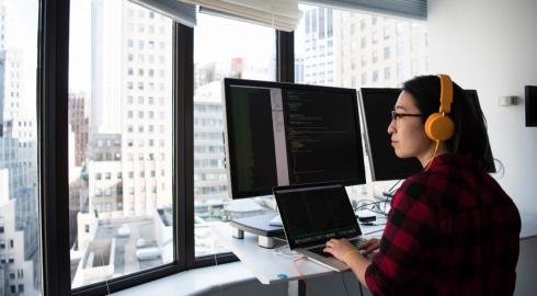 Developer coding on a multi-monitor setup with a view of the skyline outside